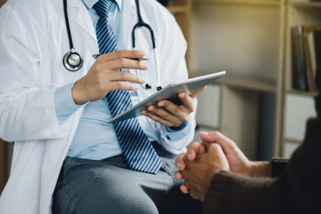 A healthcare professional in a white coat discussing medical information with a patient while holding a tablet